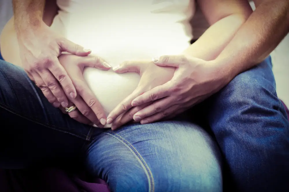 Couple with hands on pregnant belly representing surrogacy, donor agreements, and family formation law.
